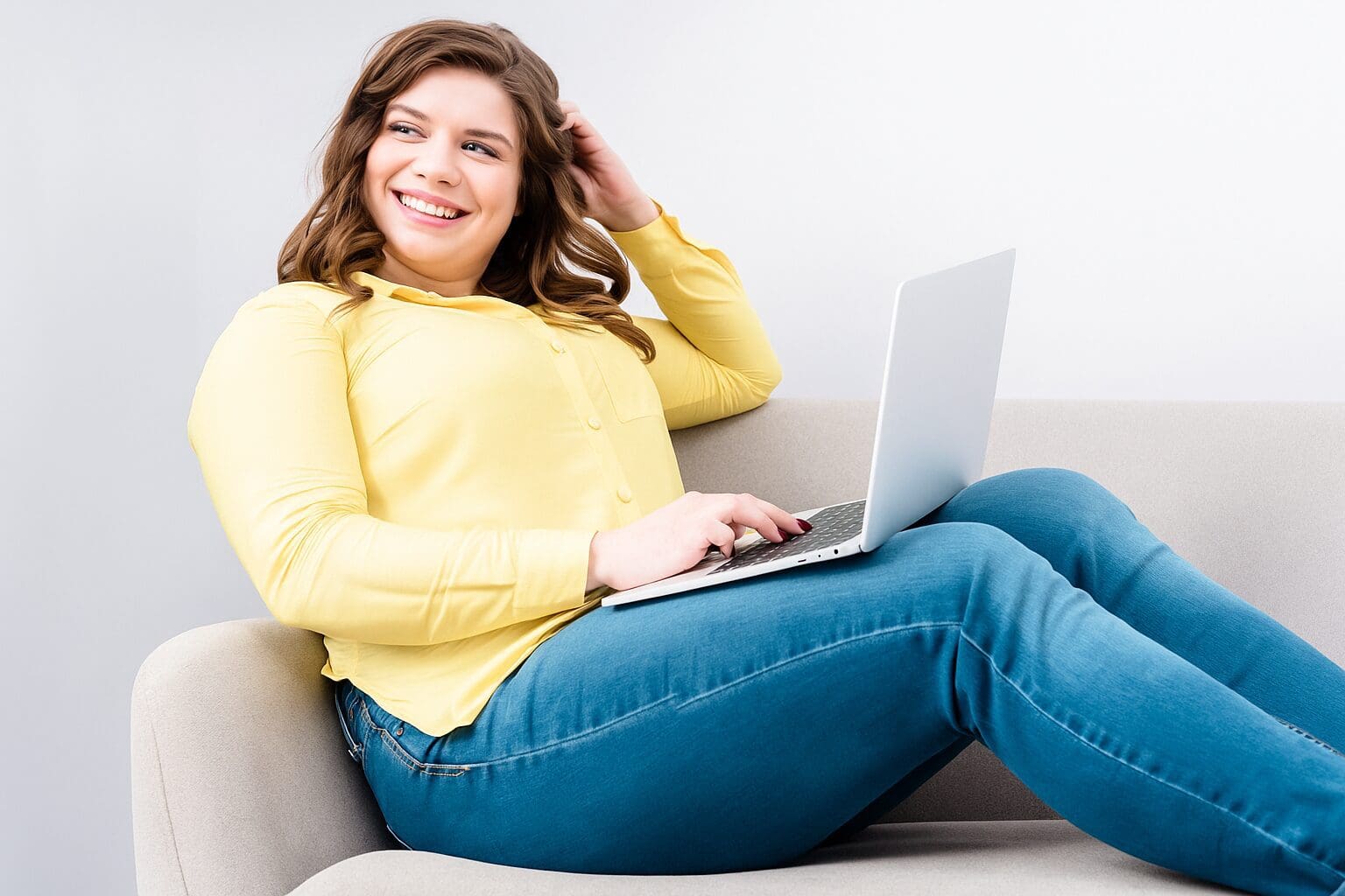 A woman in a yellow sweater working on a laptop while smiling.