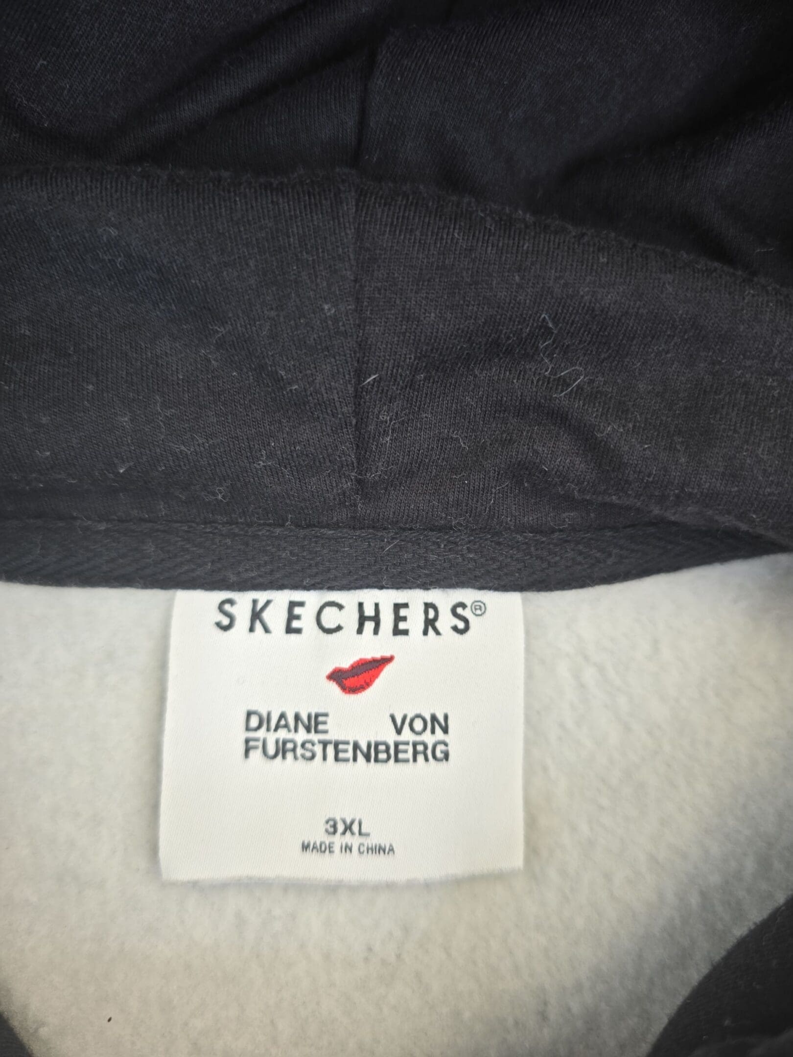 Close-up of Diane von Furstenberg x Skechers brand and 3XL size tag on black and white geometric hoodie