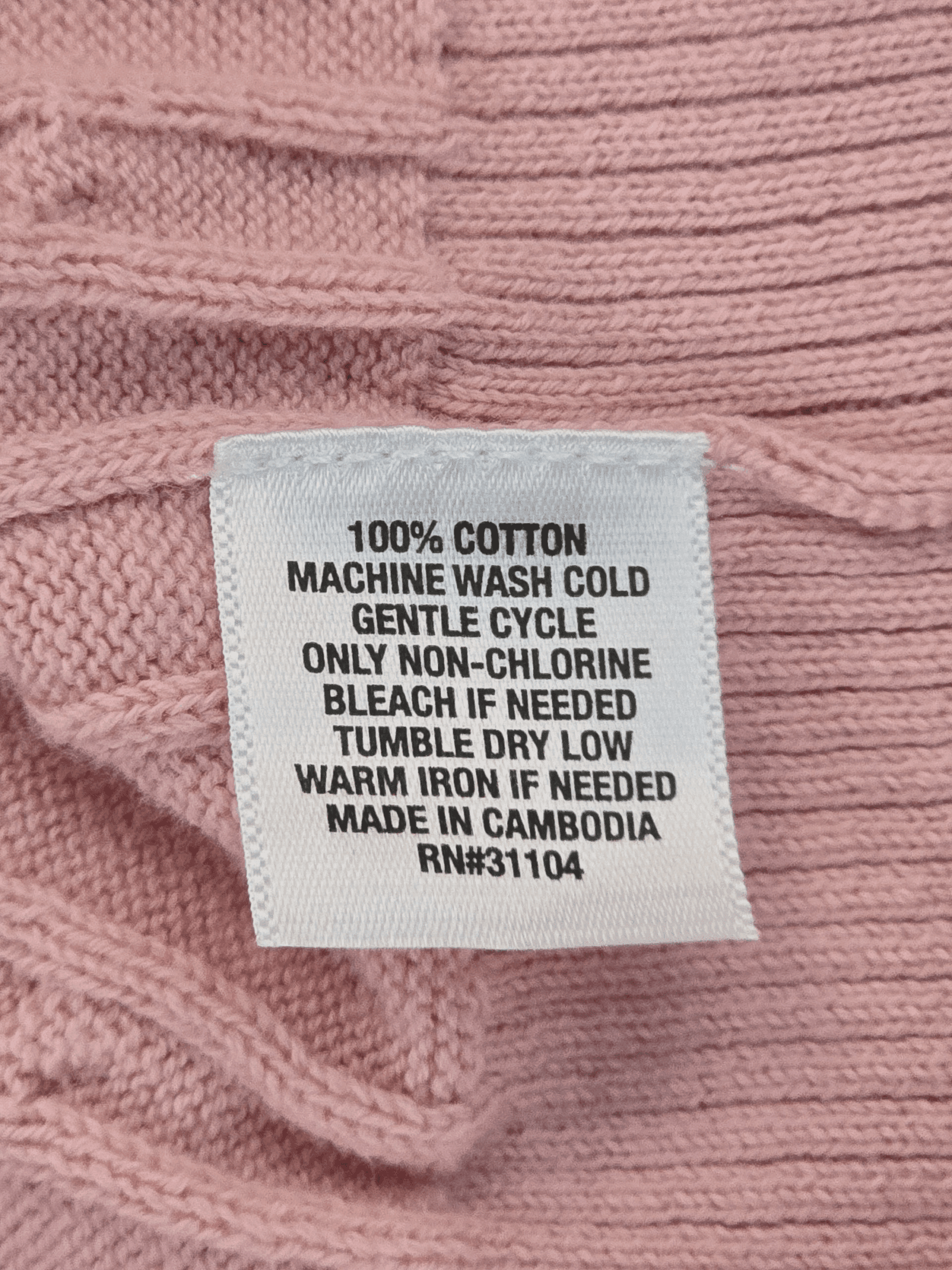 Clothing tag with washing instructions on a pink knit fabric.