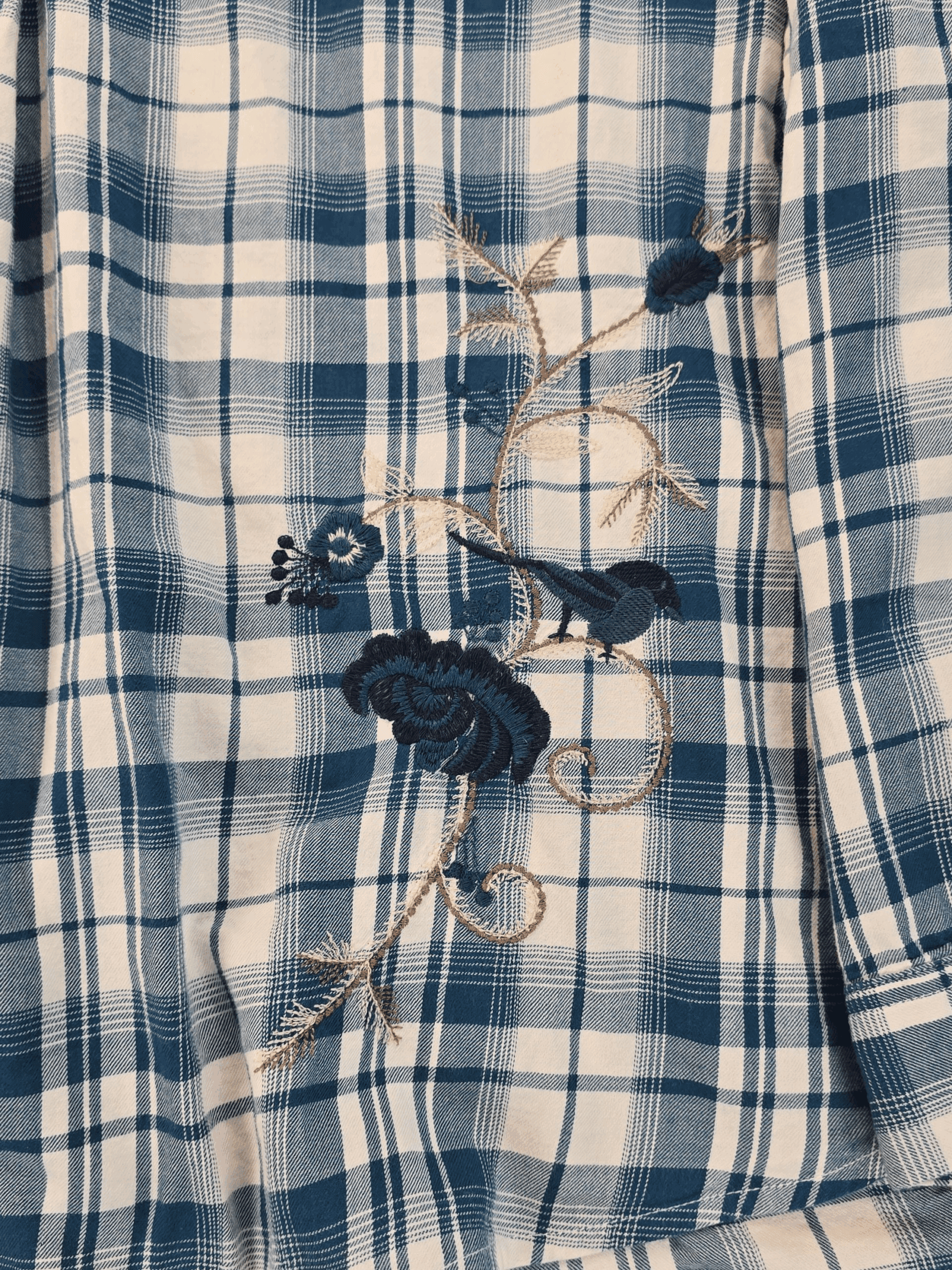 Close-up of a blue checkered shirt with embroidered bee and flower designs.