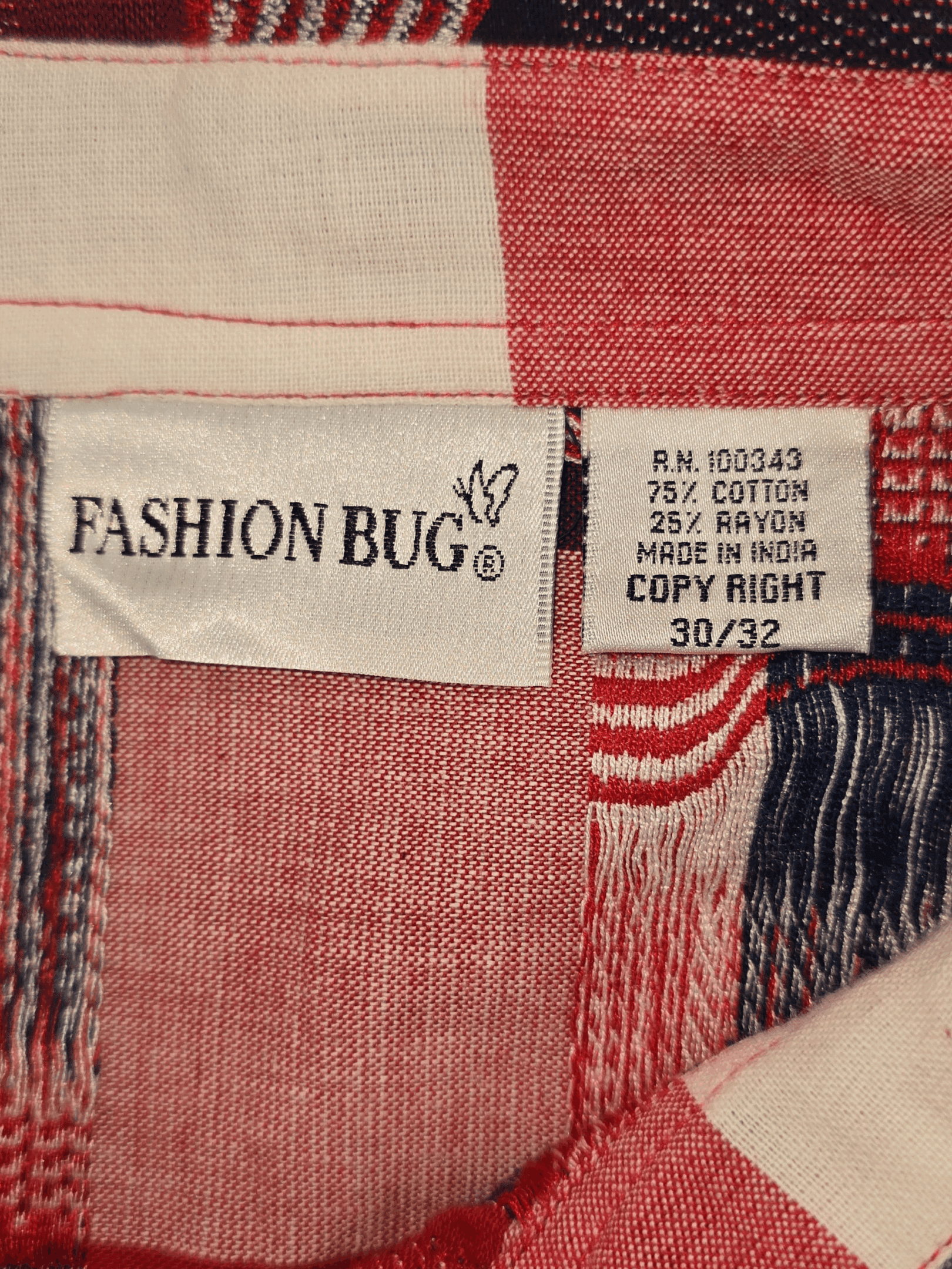 Material content tag listing cotton and polyester blend for Fashion Bug red, white, and blue American flag plaid button-up shirt.