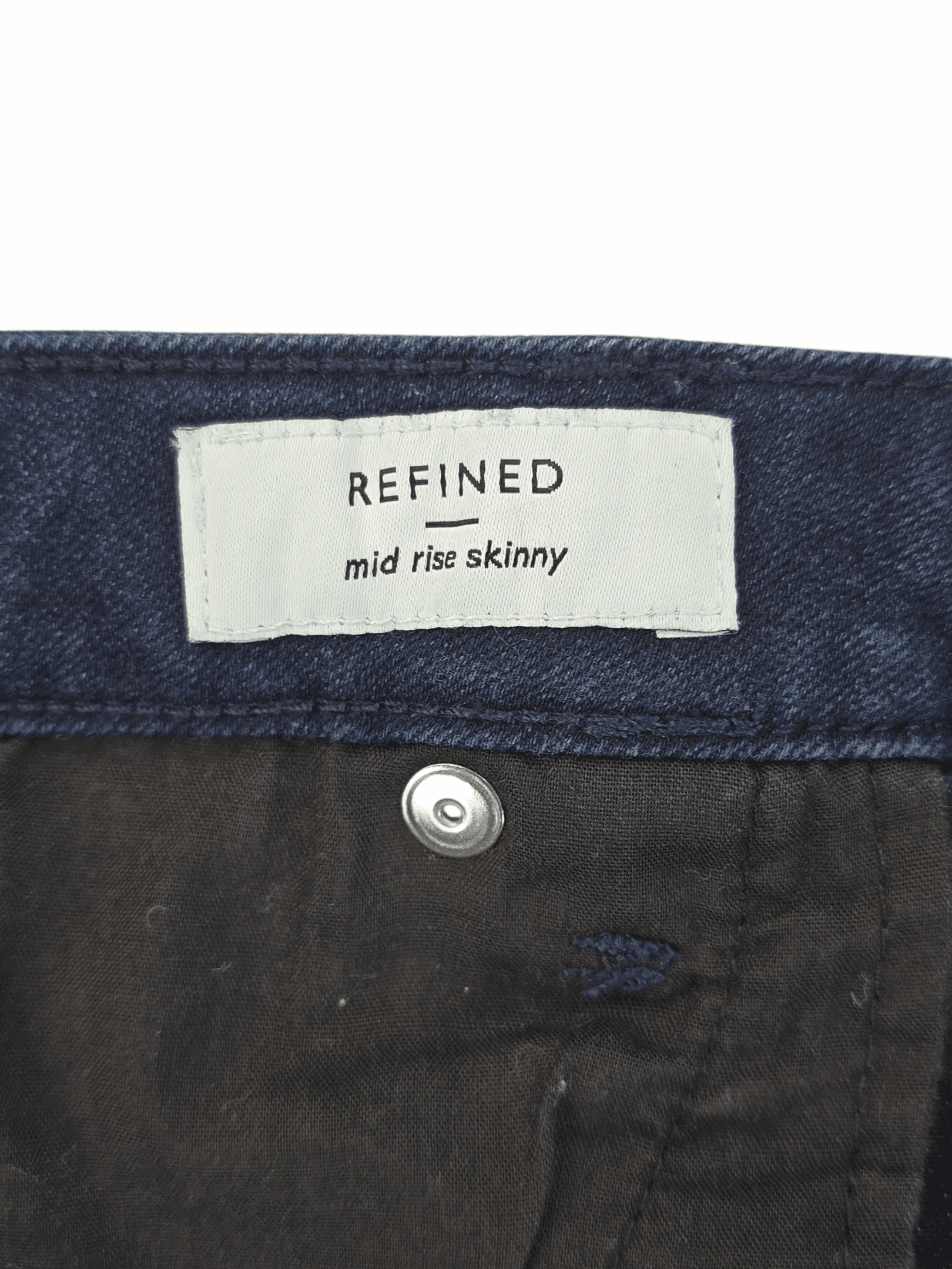 Label inside dark denim jeans reading 'REFINED mid rise skinny'.