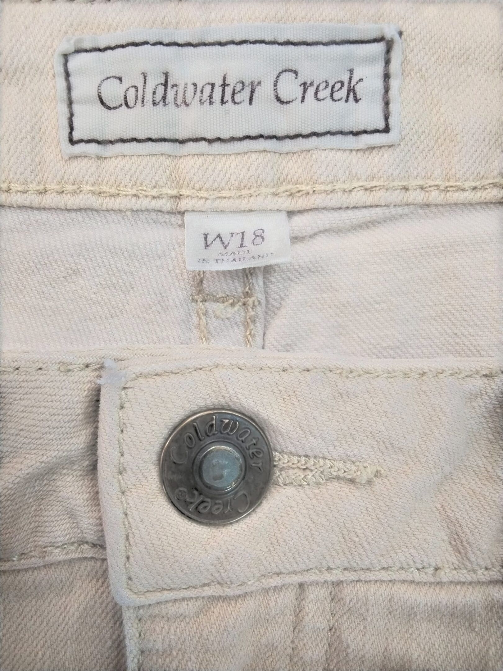 Close-up of a beige Colavater Creek pants label and button.