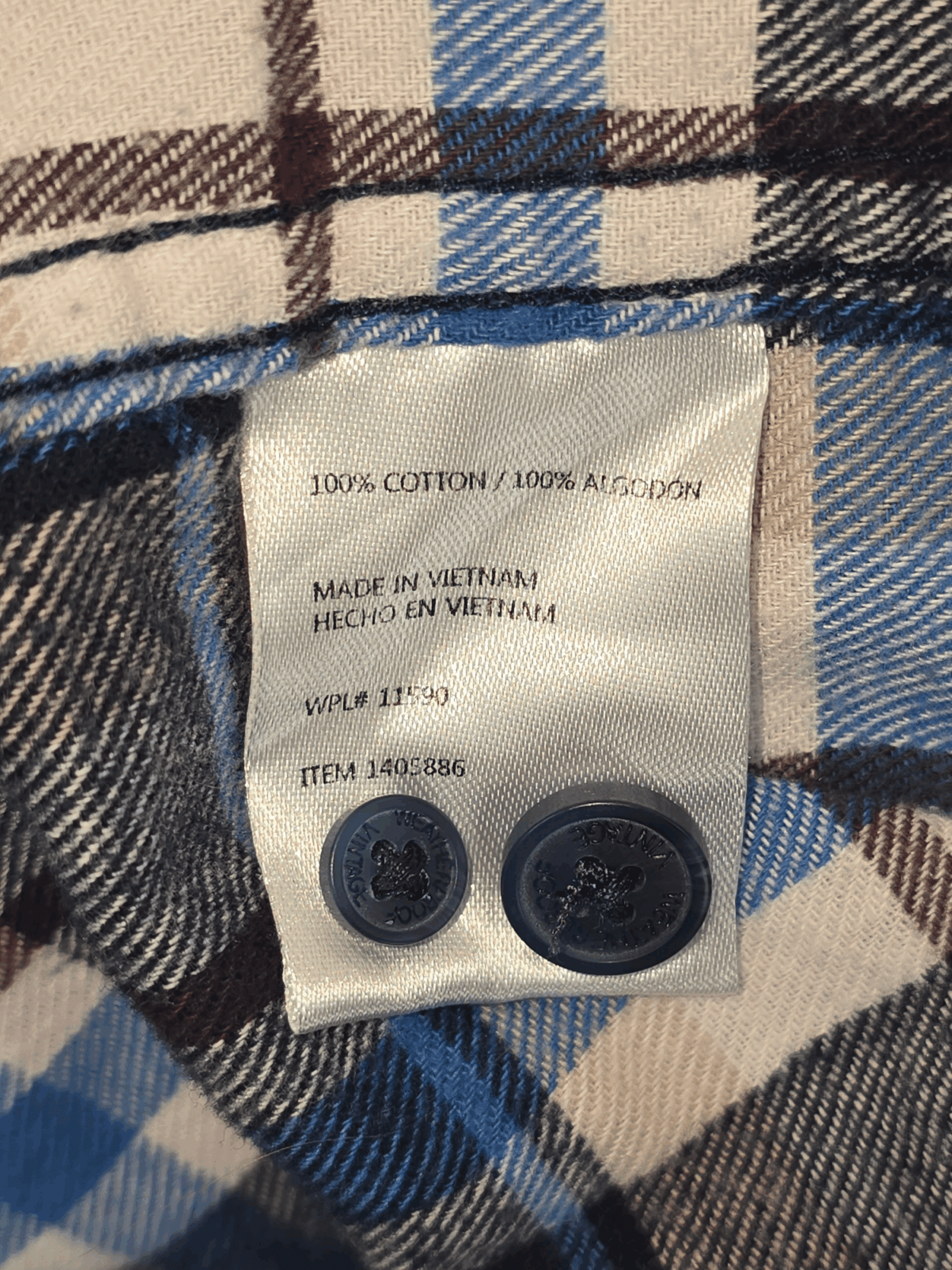 Clothing label showing material and origin with two attached buttons.