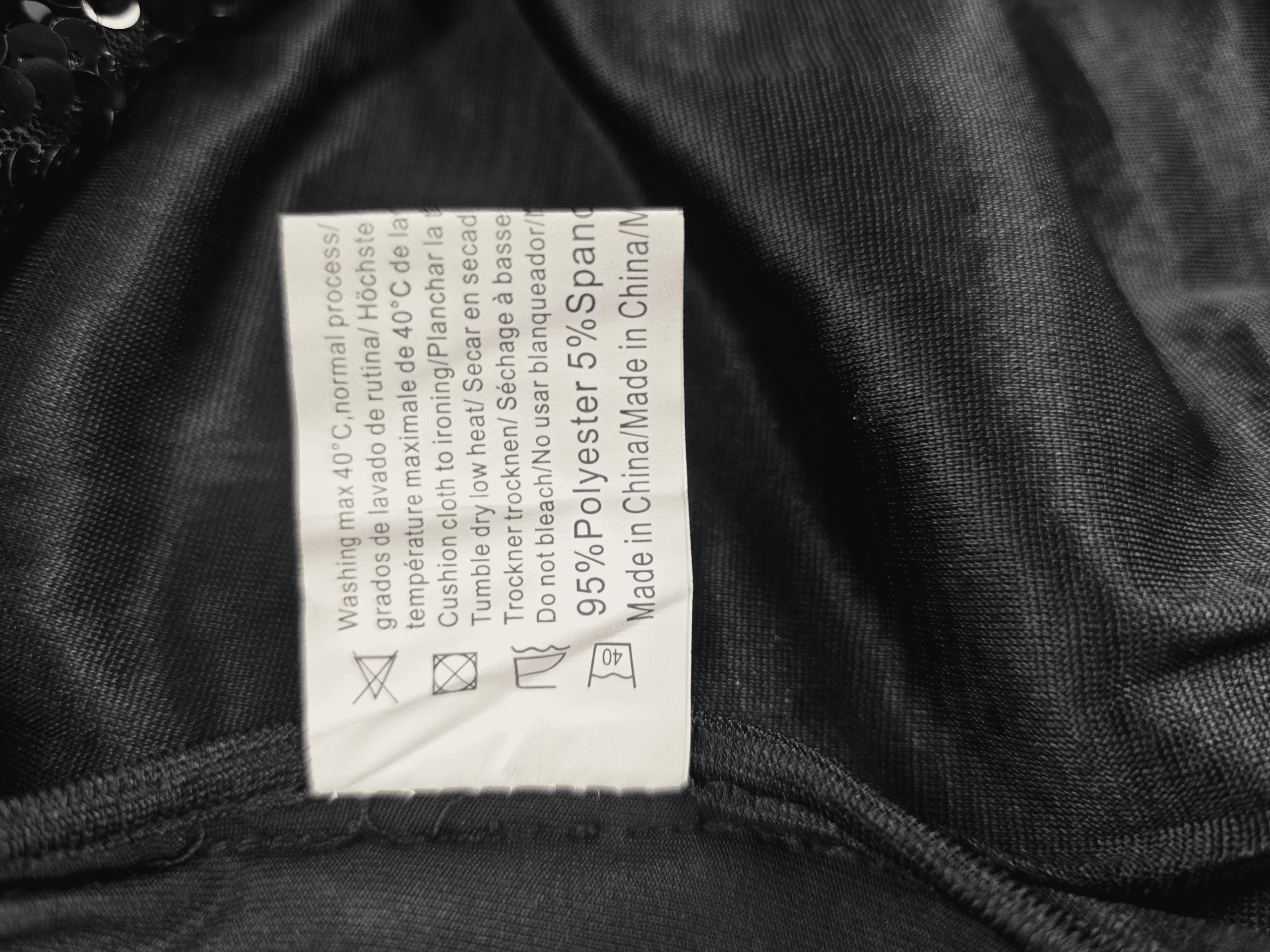 Clothing label with text and care symbols on a dark fabric background.