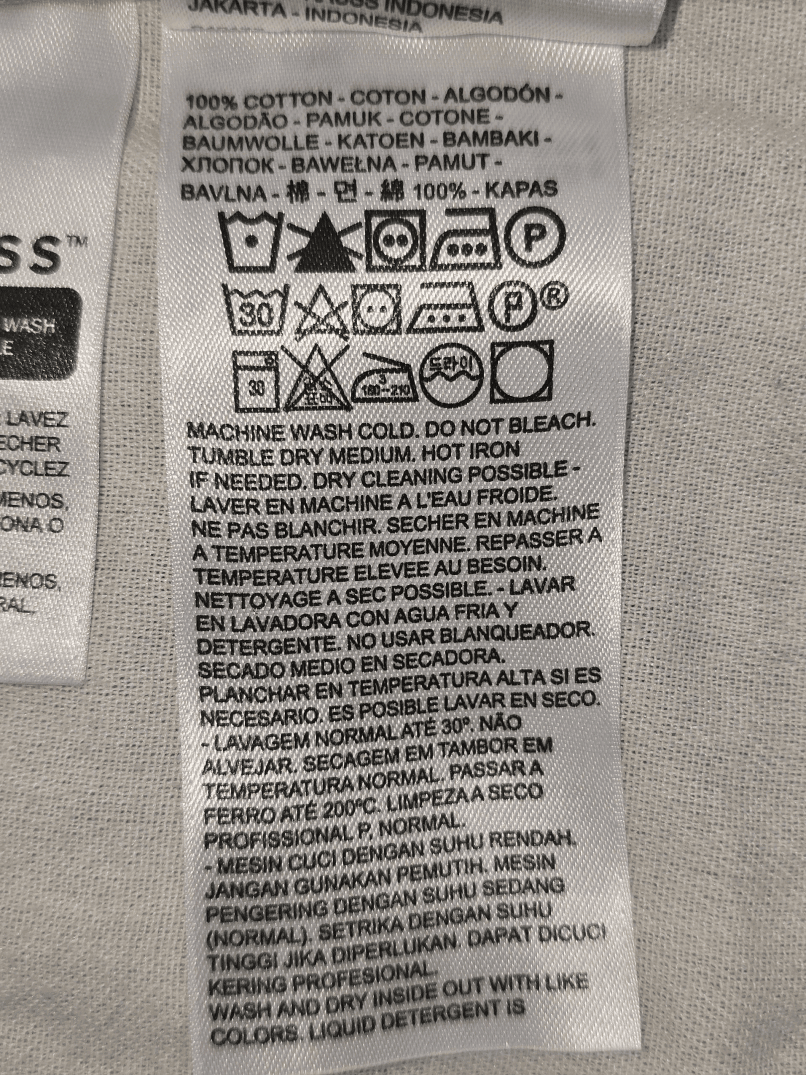 Clothing care label with washing, drying, and ironing instructions in multiple languages.