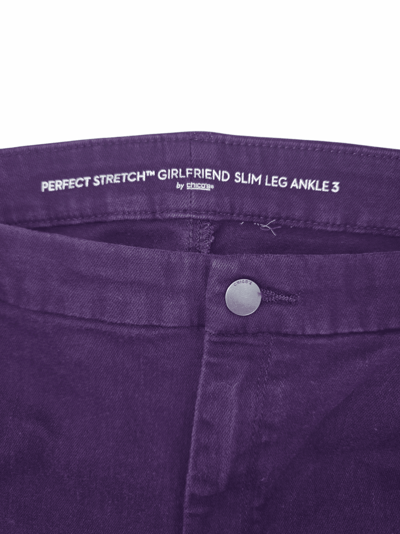 Close-up of purple jeans with a button and label inside the waistband.