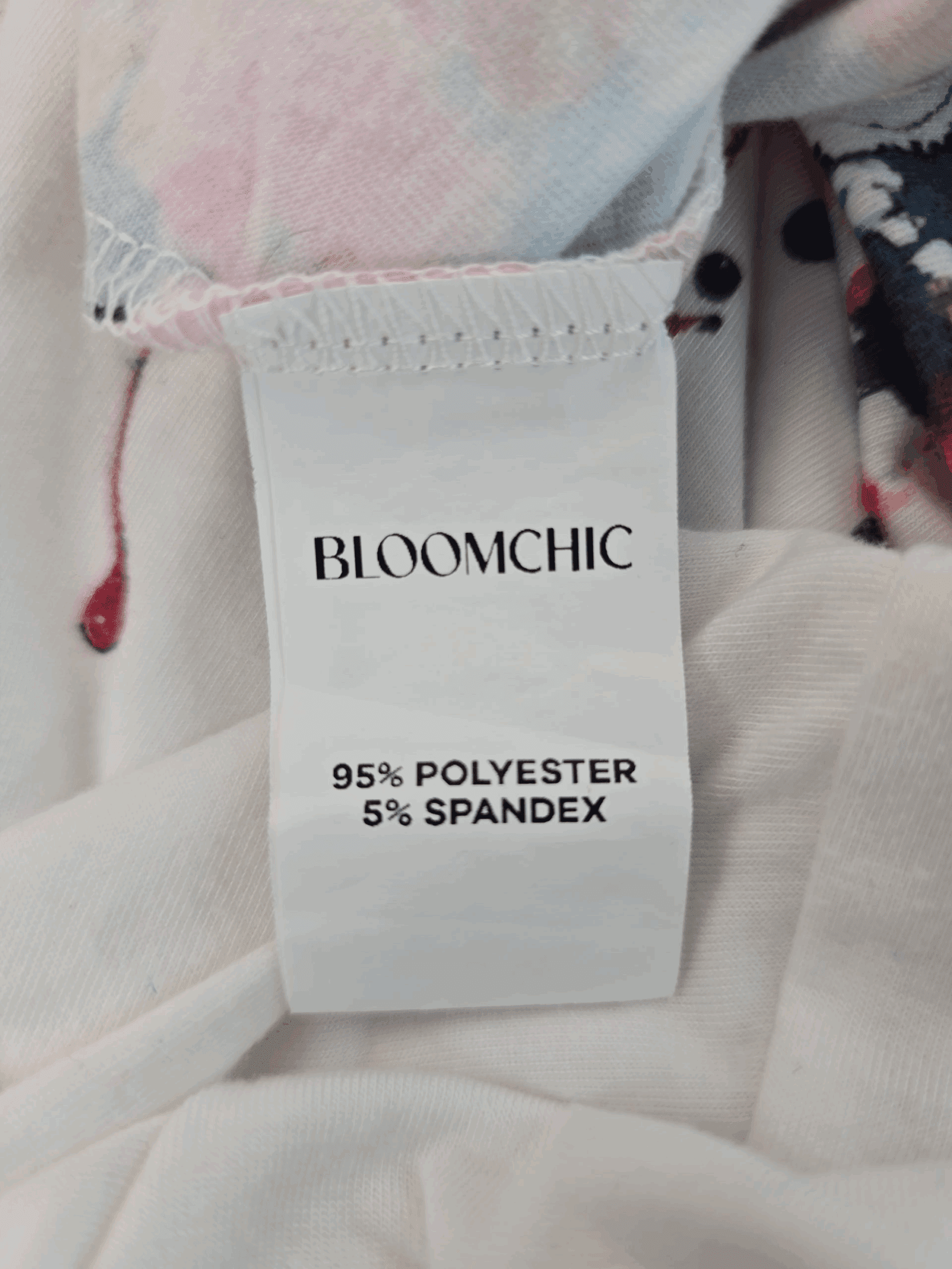 Material content tag listing polyester and spandex blend for Bloom Chic multi-color paint splatter V-neck pullover top.