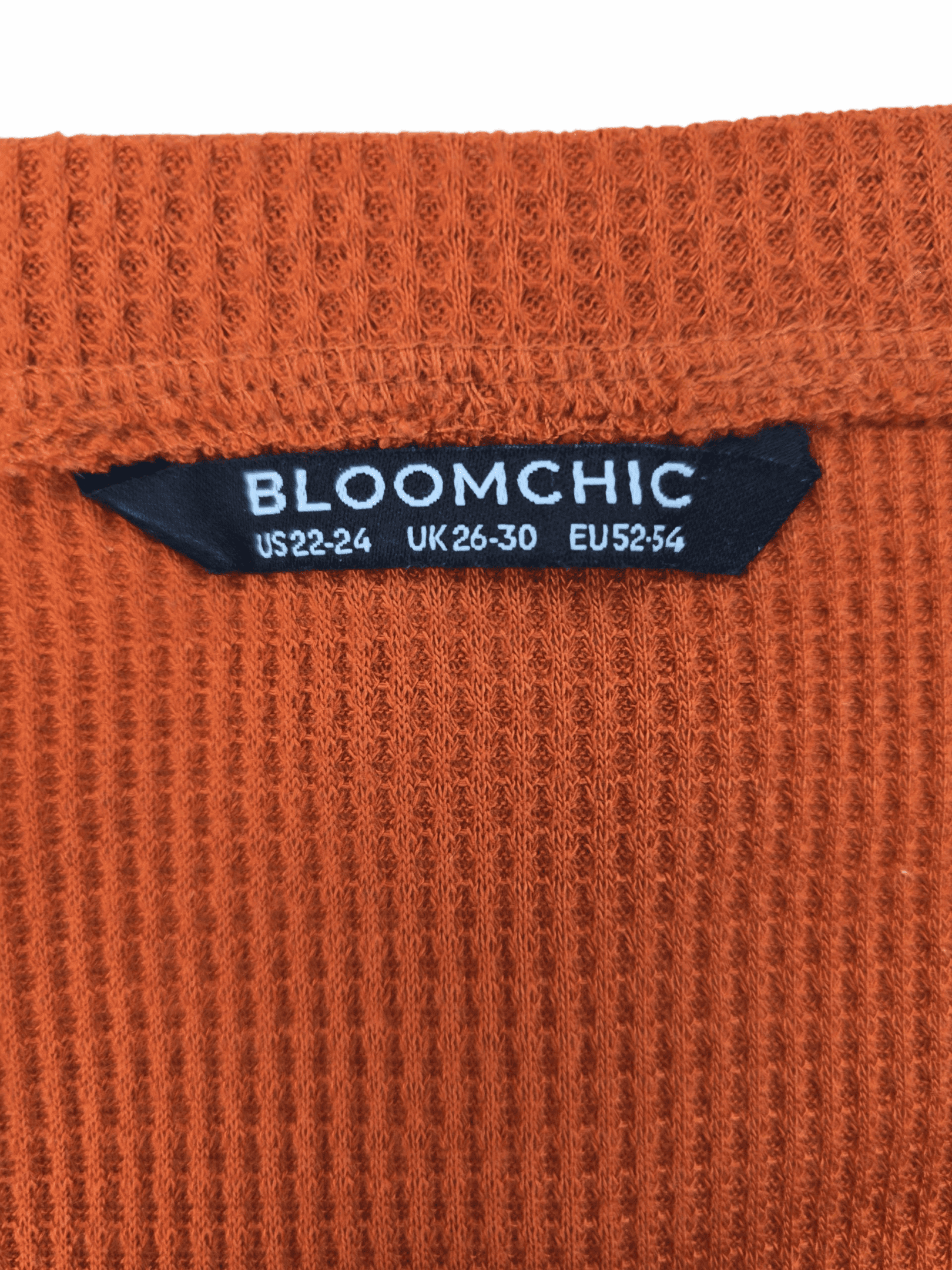 Close-up of a Bloomchic clothing label on an orange knitted fabric.