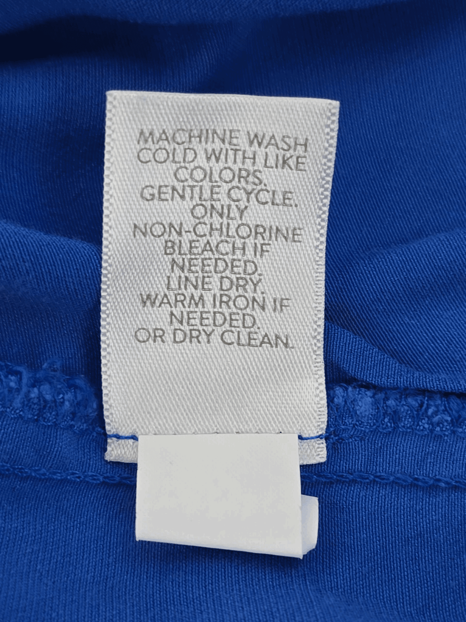 Clothing care label with washing instructions on blue fabric.