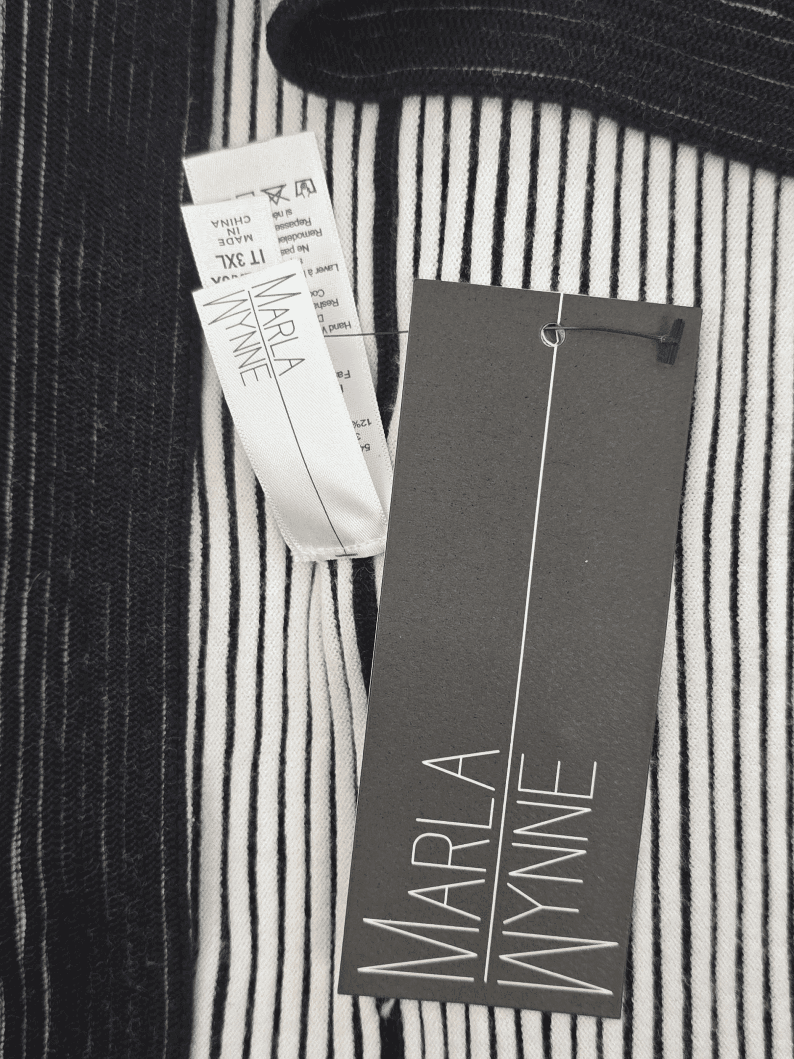 Clothing tags on a black and white striped fabric.