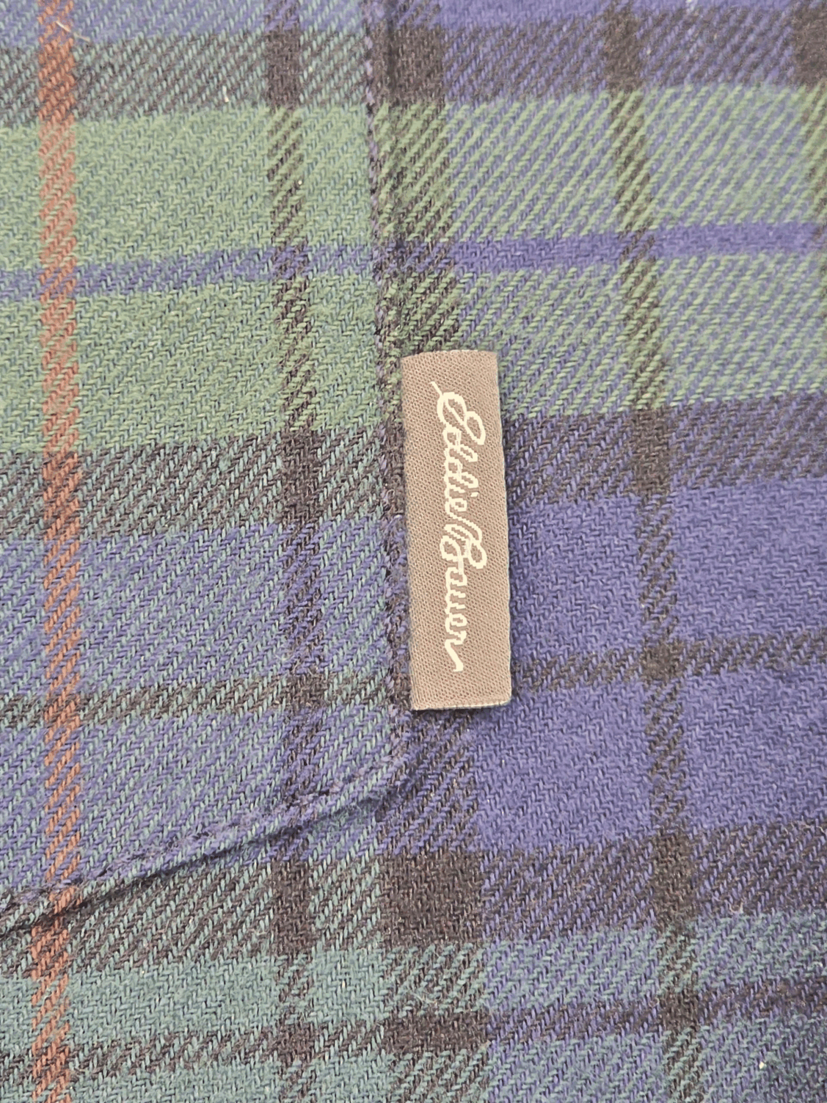 Eddie Bauer Close-up of a beige Eddie Bauer tag on blue and green plaid fabric.