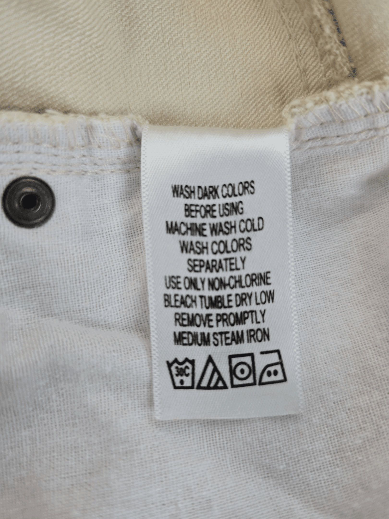 Clothing care label with washing and drying instructions on white fabric.