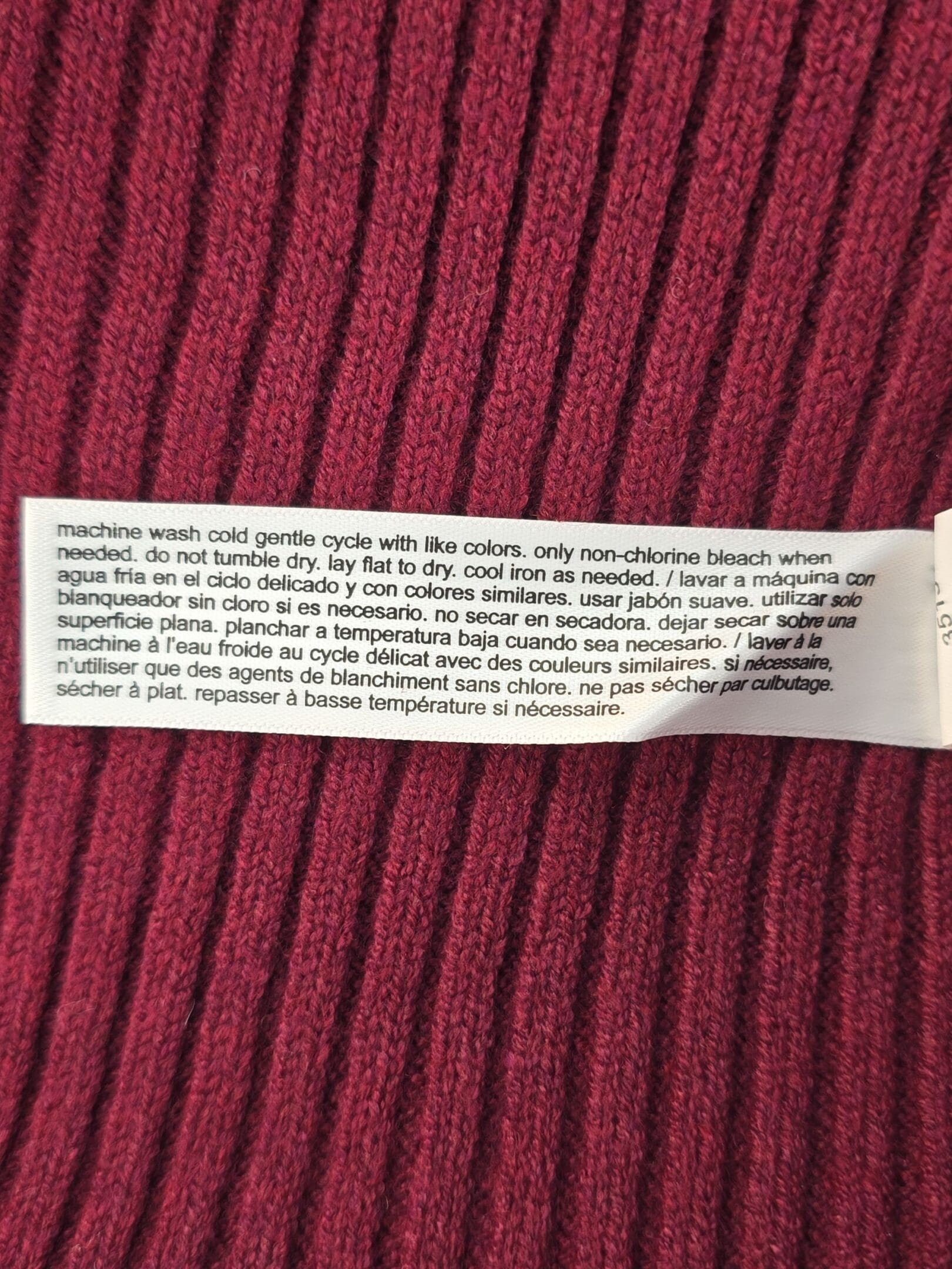 Close-up of a clothing care label with washing instructions on a red ribbed fabric.