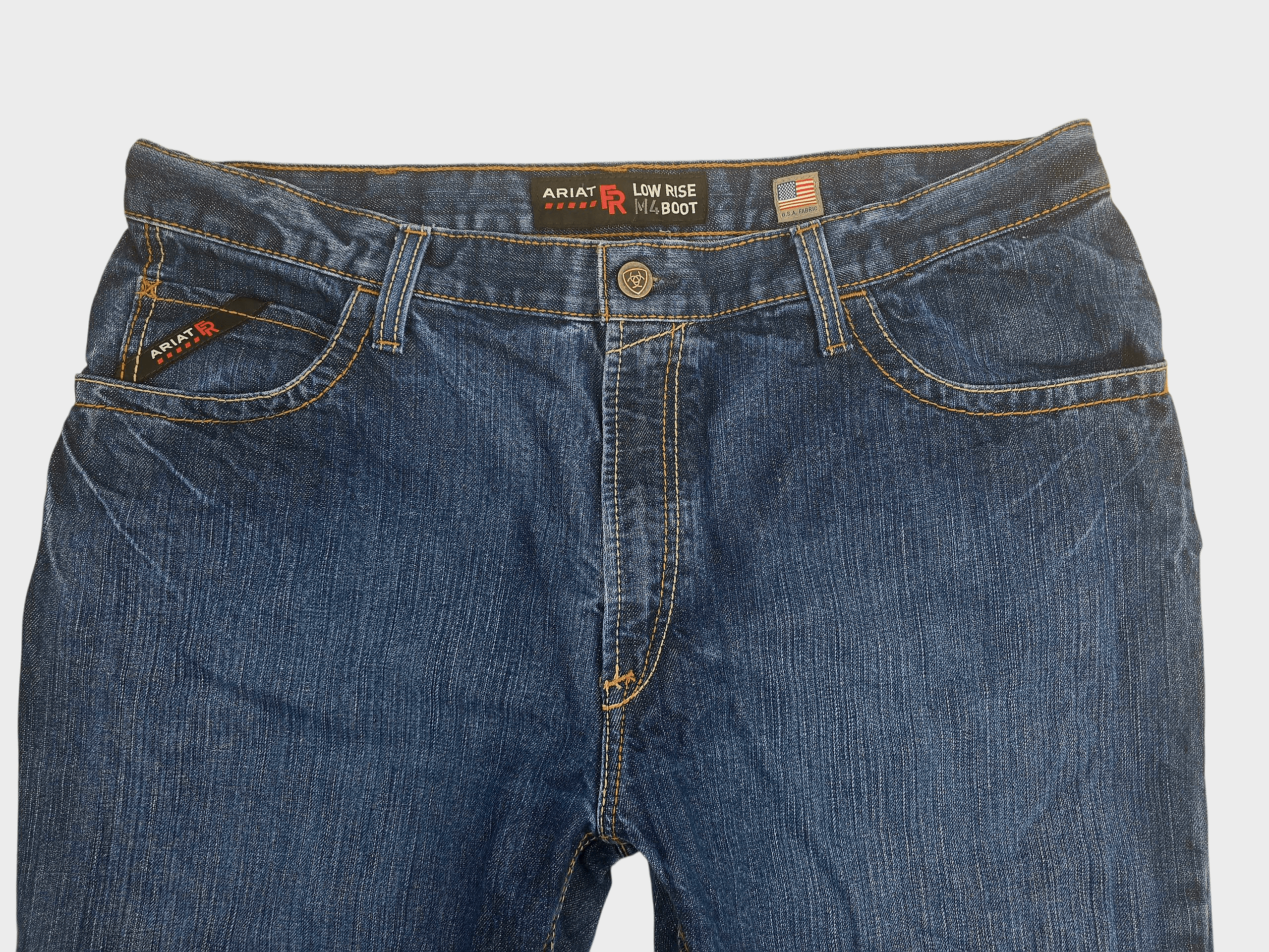 Close-up of front of Ariat men’s size 40x32 M4 FR low-rise bootcut jeans showing waistband, button, and pocket detail
