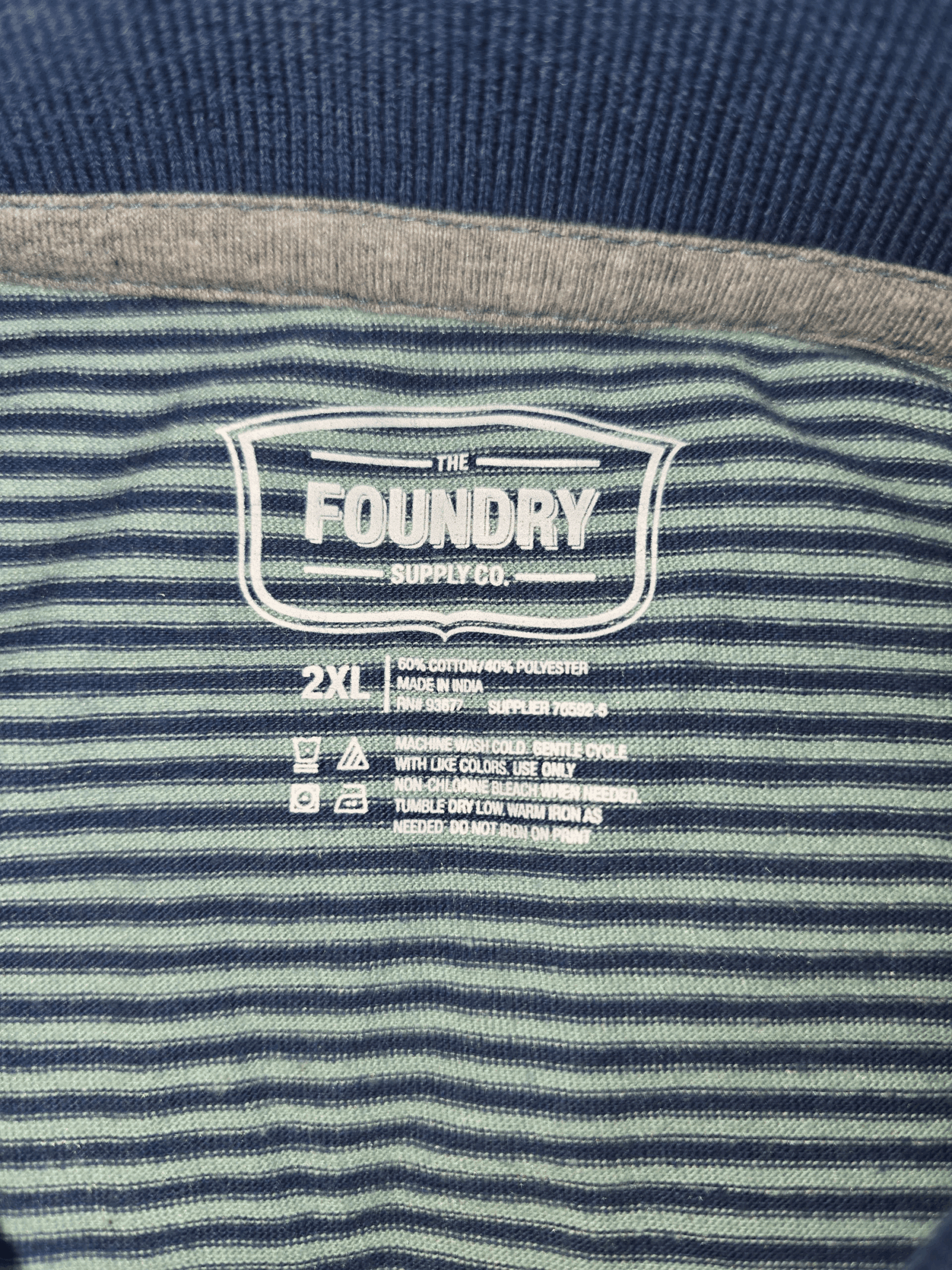 Close-up of The Foundry brand and 2XL size tag on navy and aqua blue striped polo shirt