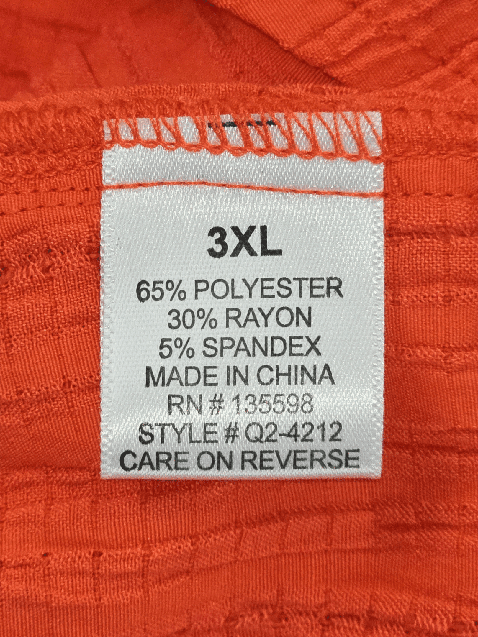 Close-up of material content and garment care tag on Cure women’s 3XL textured orange pullover top