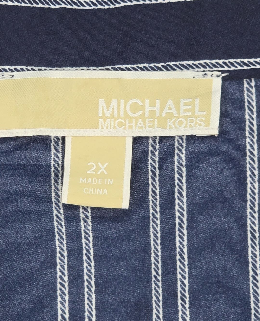 Close-up of Michael Kors brand and 2X size tag on navy blue gold-zip shirt